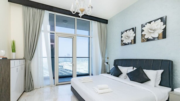 Una camera da letto moderna con un grande letto, vista sul mare attraverso finestre a tutta parete e un lampadario.