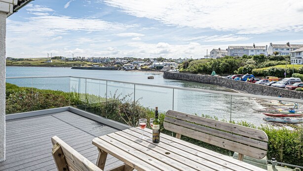 Une terrasse en bois avec une table et un banc, d’où l’on a vue sur un port, avec des bateaux et des bâtiments en arrière-plan.