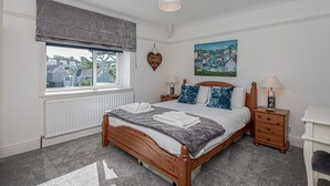 Une chambre avec un grand lit, une fenêtre donnant sur un beau paysage, une table de chevet avec une lampe et un tableau accroché au mur.