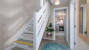 Una escalera moderna con barandillas blancas y una franja amarilla de seguridad, que conduce a una cocina con una mesa y sillas.
