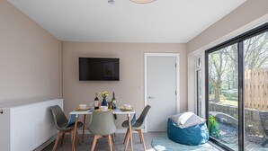 Un comedor con una mesa dispuesta para cuatro personas, un televisor montado en la pared y un amplio ventanal con vistas al exterior.