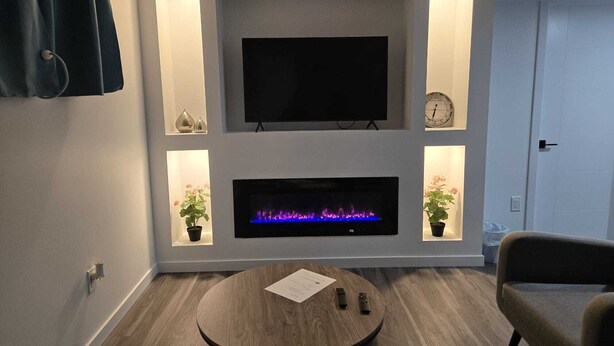 Un soggiorno moderno con una televisione a schermo piatto sopra un caminetto, affiancato da due piccole mensole con oggetti decorativi.