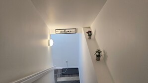 Una scala con un cartello che recita 'Welcome' in cima, un lampadario a parete e due piante in vaso su entrambi i lati.