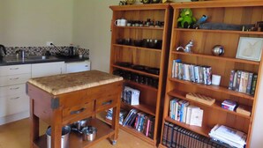 A kitchen with a wooden table, shelves with books and toys, and a sink. - Nut Cottage (Whanganui)
