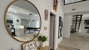 A modern interior with a large mirror, a wooden console table with a sign, and a staircase leading to an upper level. - Cozy Luxury  Pool + Home Theater + Backyard Oasis (San Antonio)