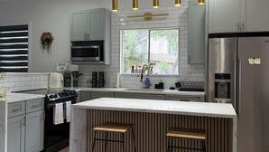 A modern kitchen with a central island, stainless steel appliances, and pendant lighting. - Cozy Luxury  Pool + Home Theater + Backyard Oasis (San Antonio)