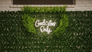 Two wicker chairs with cushions in front of a wall with a green leafy texture and a neon sign that reads "Good Vibes Only". - Cozy Luxury  Pool + Home Theater + Backyard Oasis (San Antonio)