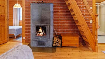 A room with a stone fireplace, a bed, a staircase, and a wooden interior.