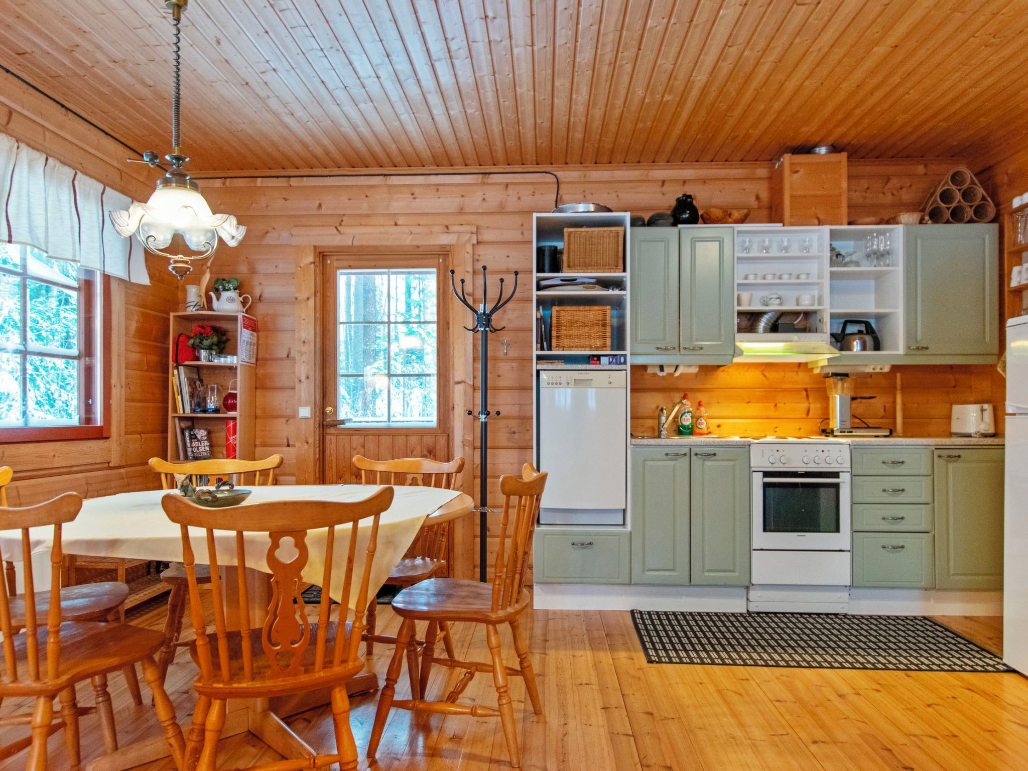 Un intérieur en bois comprenant une table à manger, des chaises, un coin cuisine avec des placards et une fenêtre.