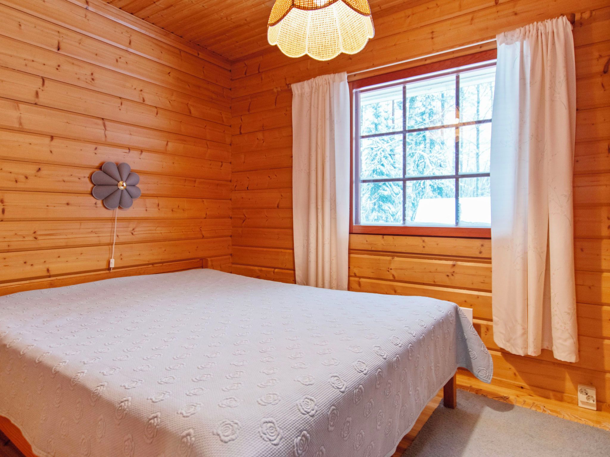 Une pièce en bois avec un lit, une fenêtre avec des rideaux et un luminaire en forme de fleur.