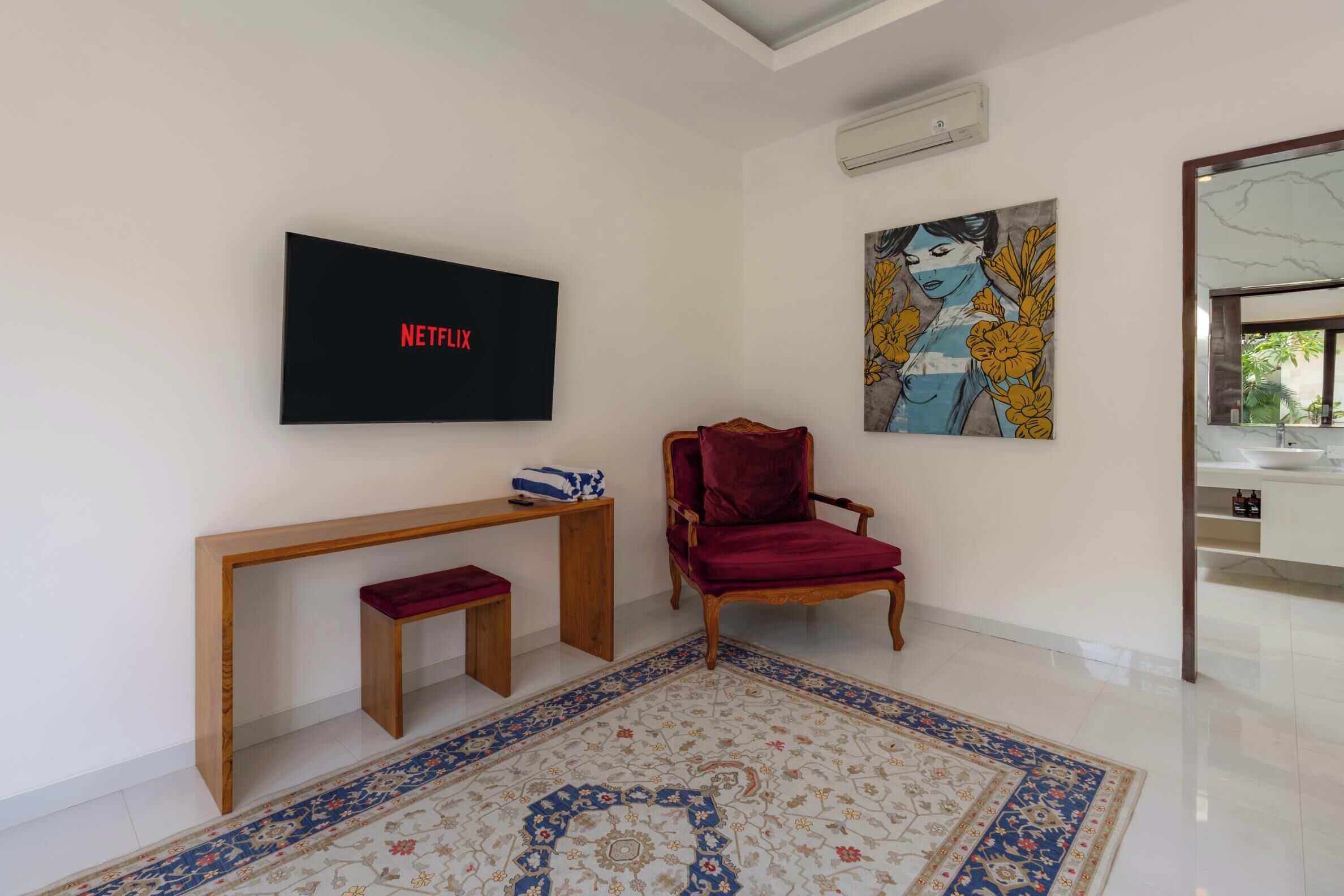 A living room with a Netflix TV, a red chair, a wooden bench, a patterned rug, and a painting on the wall.