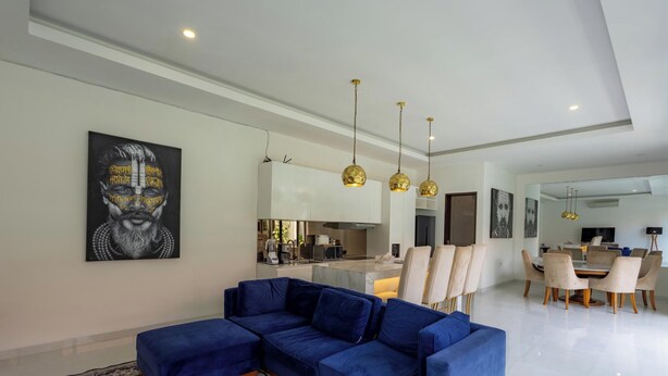 Un soggiorno moderno con un divano angolare blu, un'area pranzo con un tavolo rotondo e sedie, e una cucina sullo sfondo.