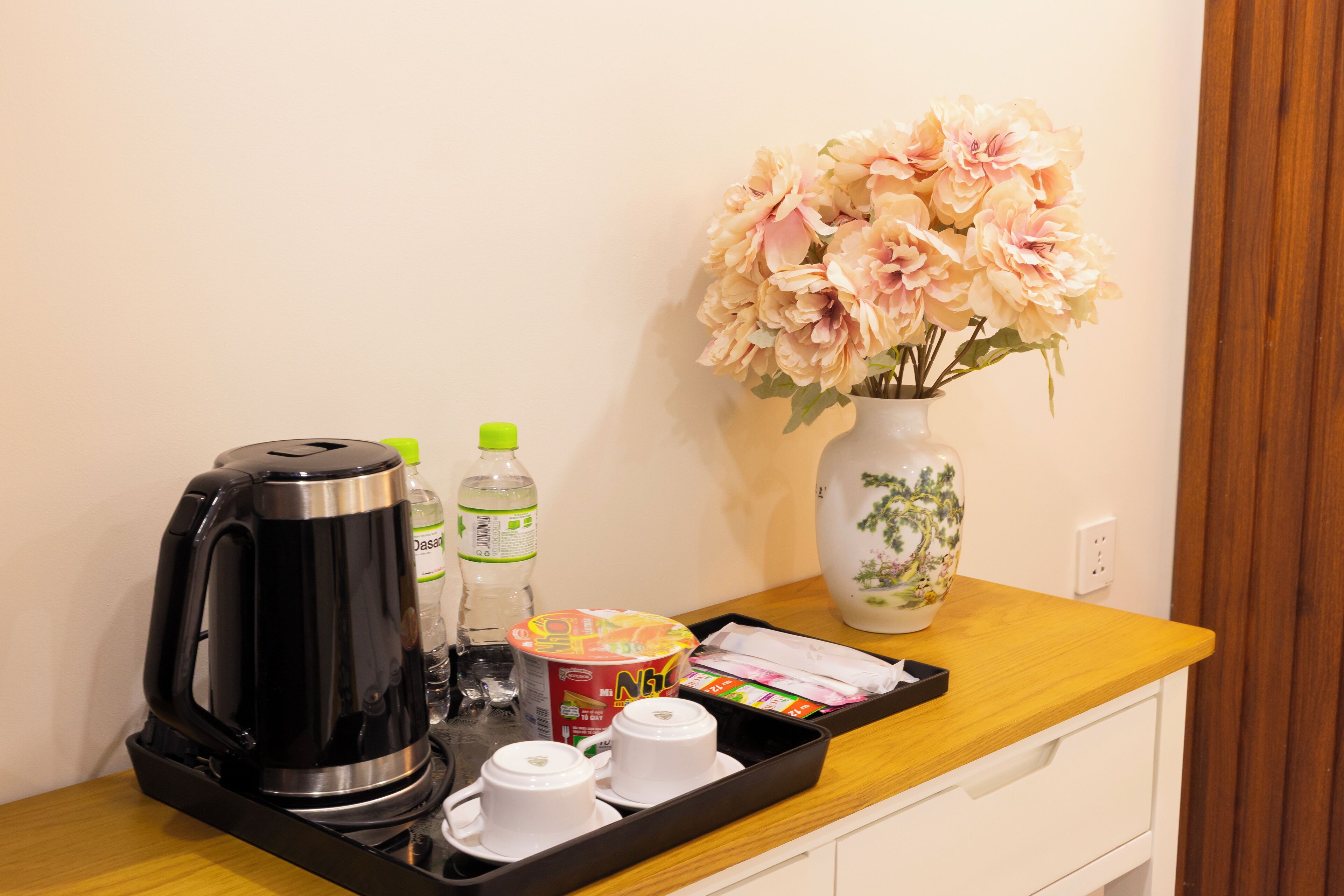 A tray with a coffee maker, water bottle, tea set, and a vase with flowers on a wooden counter.