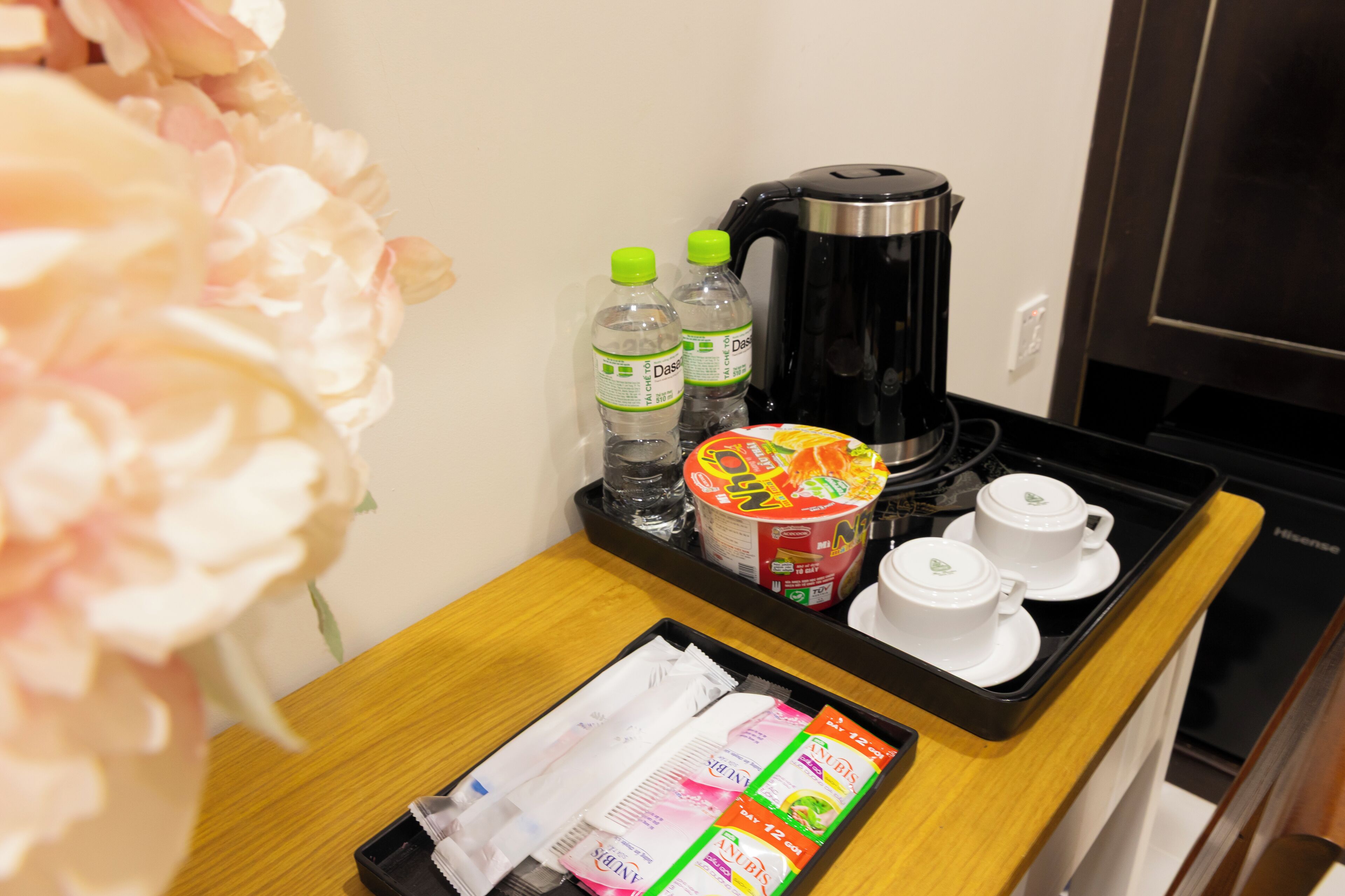 A tray with a coffee maker, two bottles of water, a box of instant noodles, two white cups, and a tray of tissues.