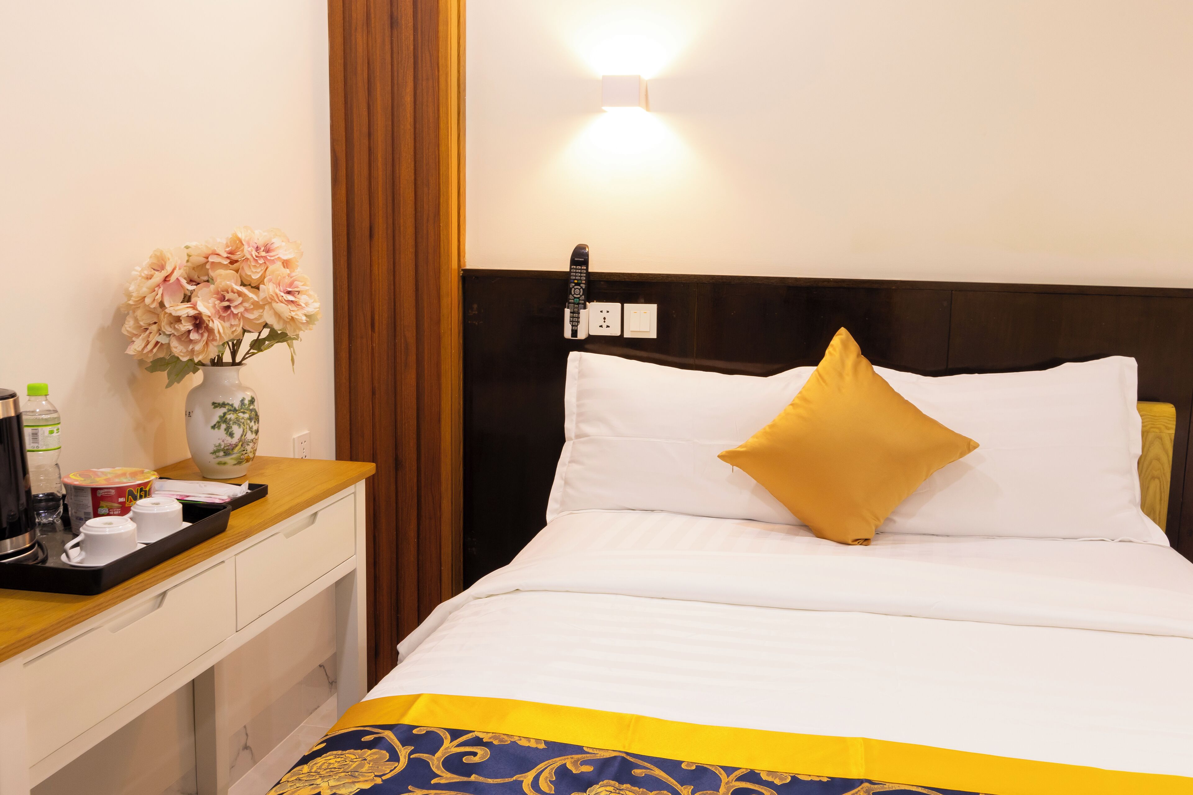 Een hotelkamer met een bed, een nachtkastje, een bloemenvaas en een dienblad met een koffiezetapparaat en bekertjes.