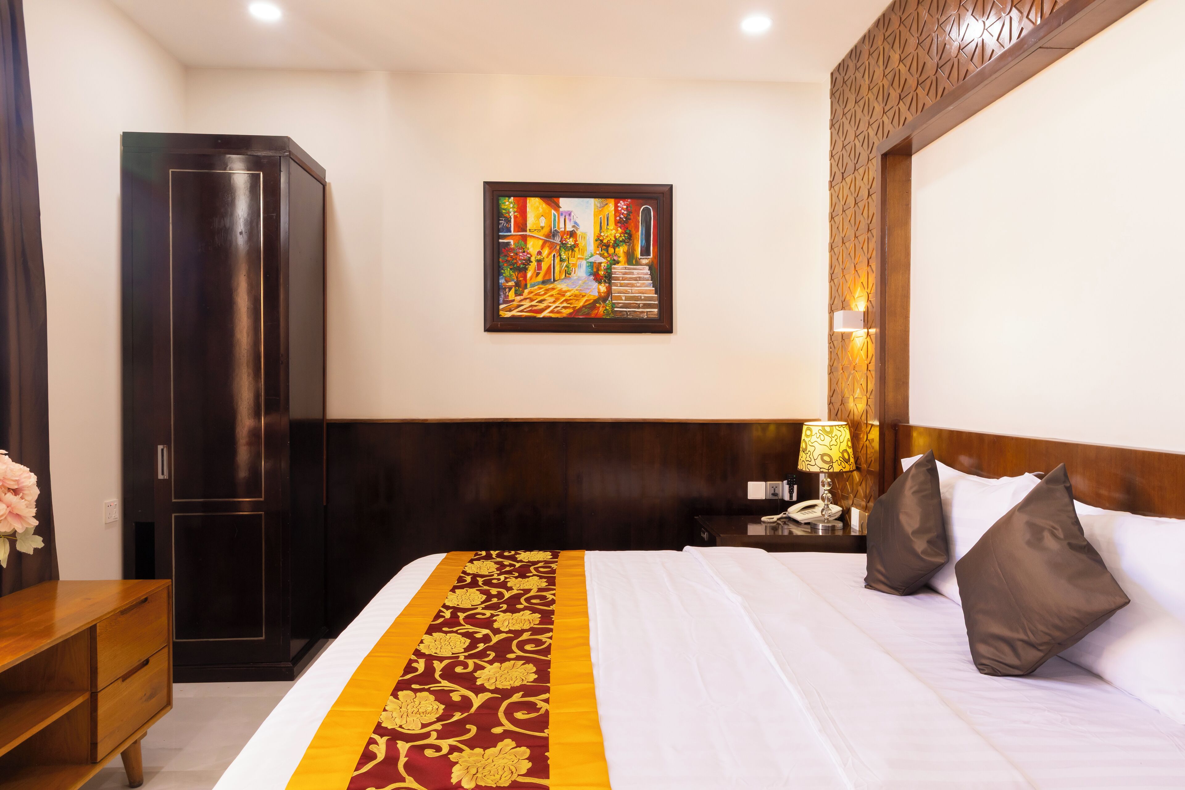 Una camera d'albergo con un letto, un comodino, una lampada, un armadio e un quadro appeso al muro.