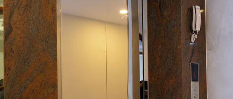 An elevator with a digital display, a phone, and potted plants.
