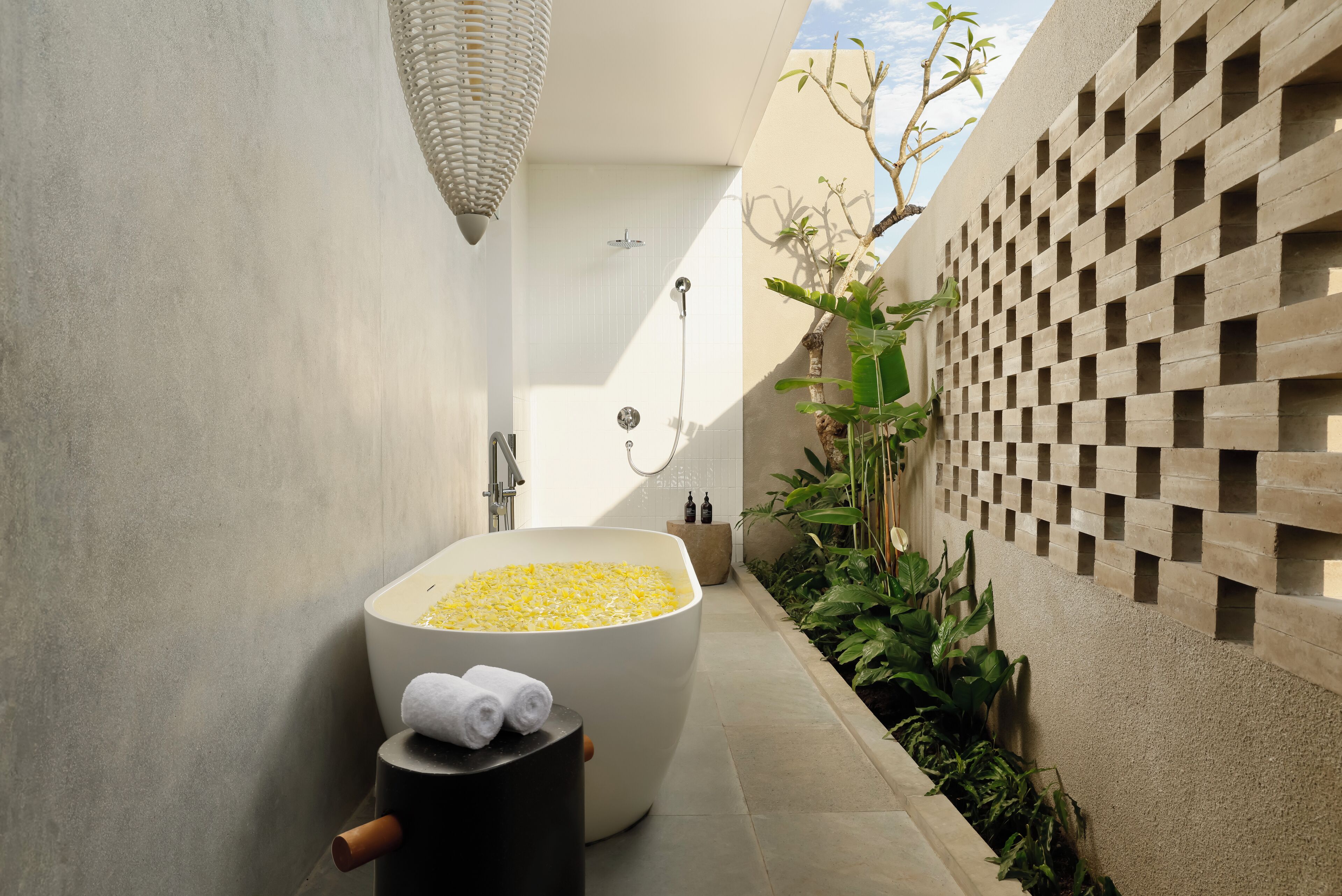 A modern bathroom with a large bathtub filled with yellow bath salts, a towel rack, and a shower area.