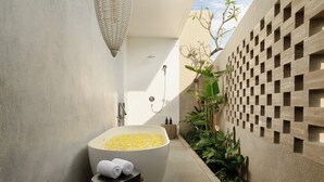 A modern bathroom with a large bathtub filled with yellow bath salts, a towel rack, and a shower area. - Uma Santai Villa Canggu by Nakula (Canggu)