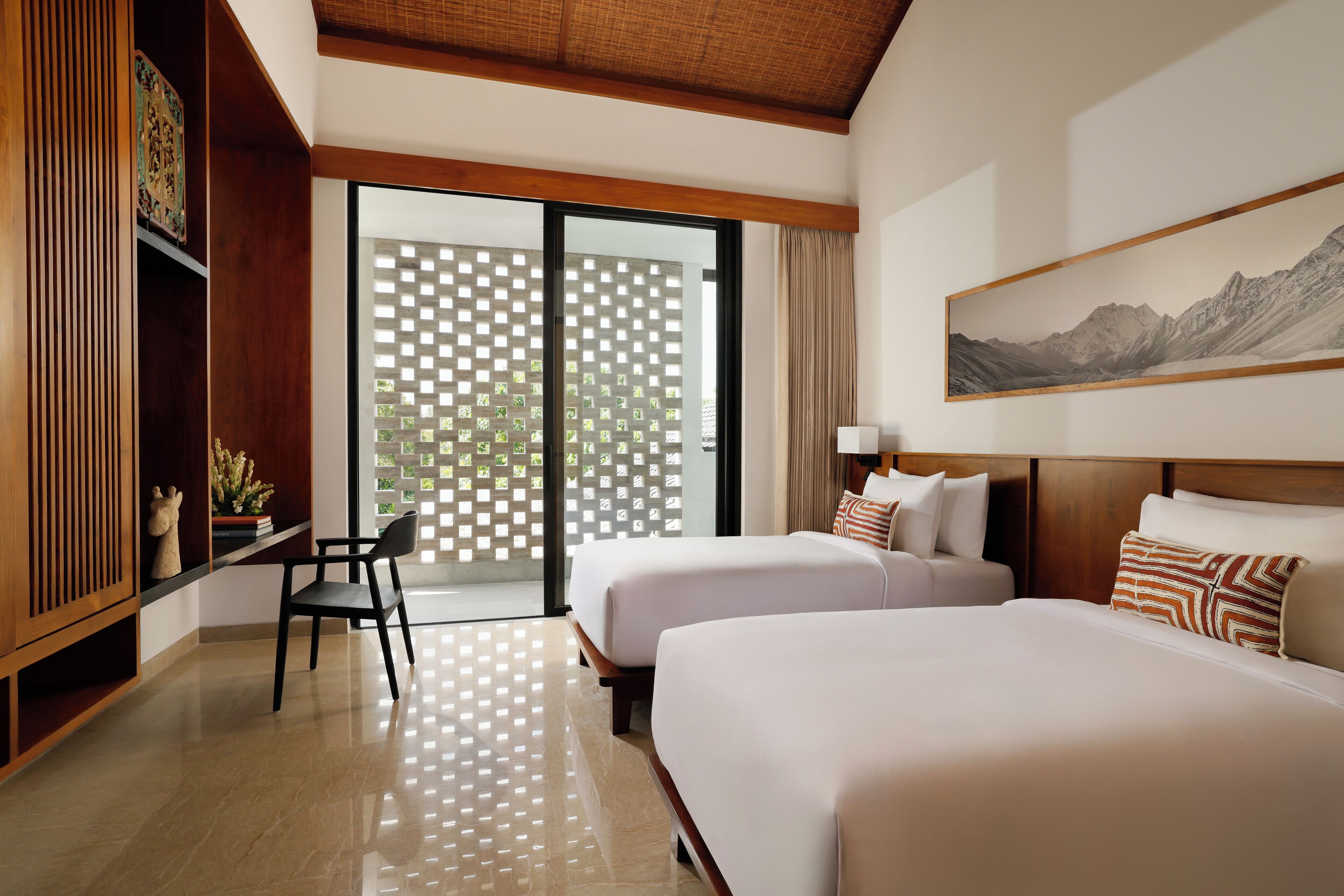 Quarto de hotel com duas camas, uma escrivaninha e uma cadeira. Uma janela grande oferece vista para o verde lá fora.