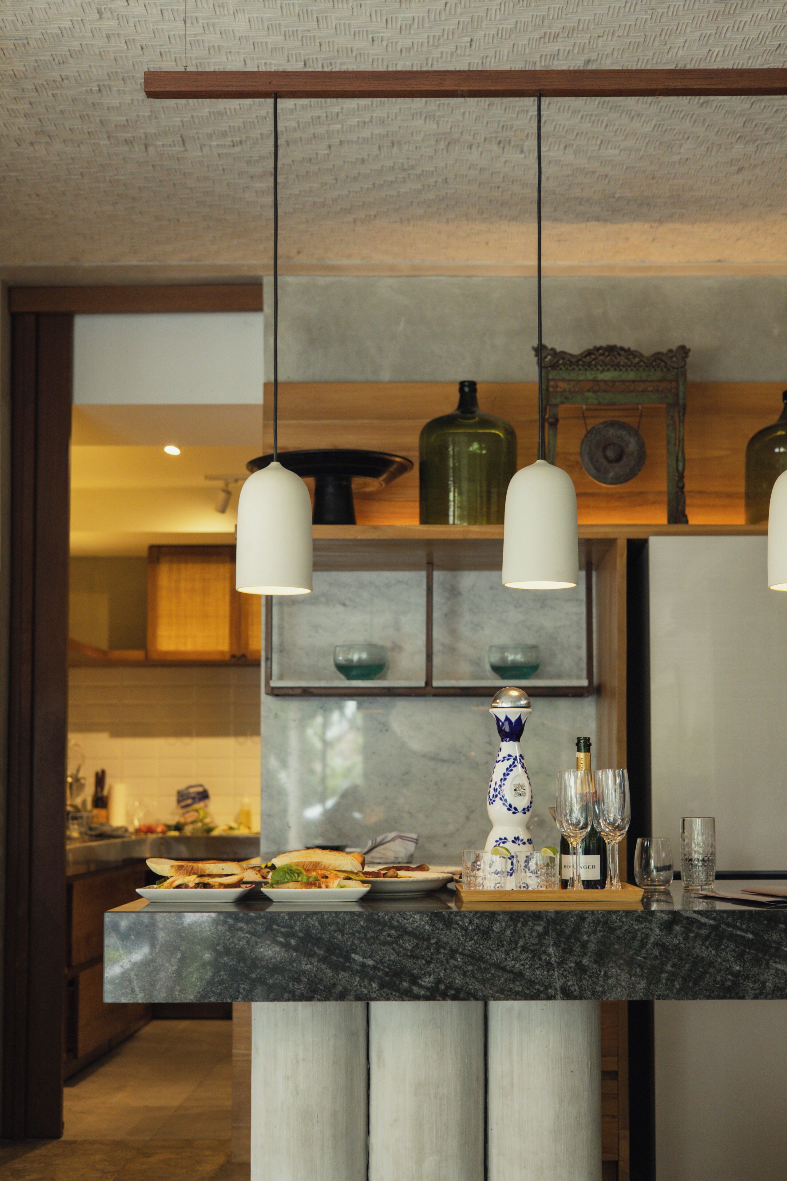 A modern kitchen with a marble countertop, hanging pendant lights, and a decorative vase.