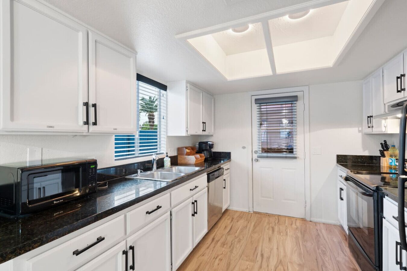 A modern kitchen with white cabinets, a black countertop, and a skylight.