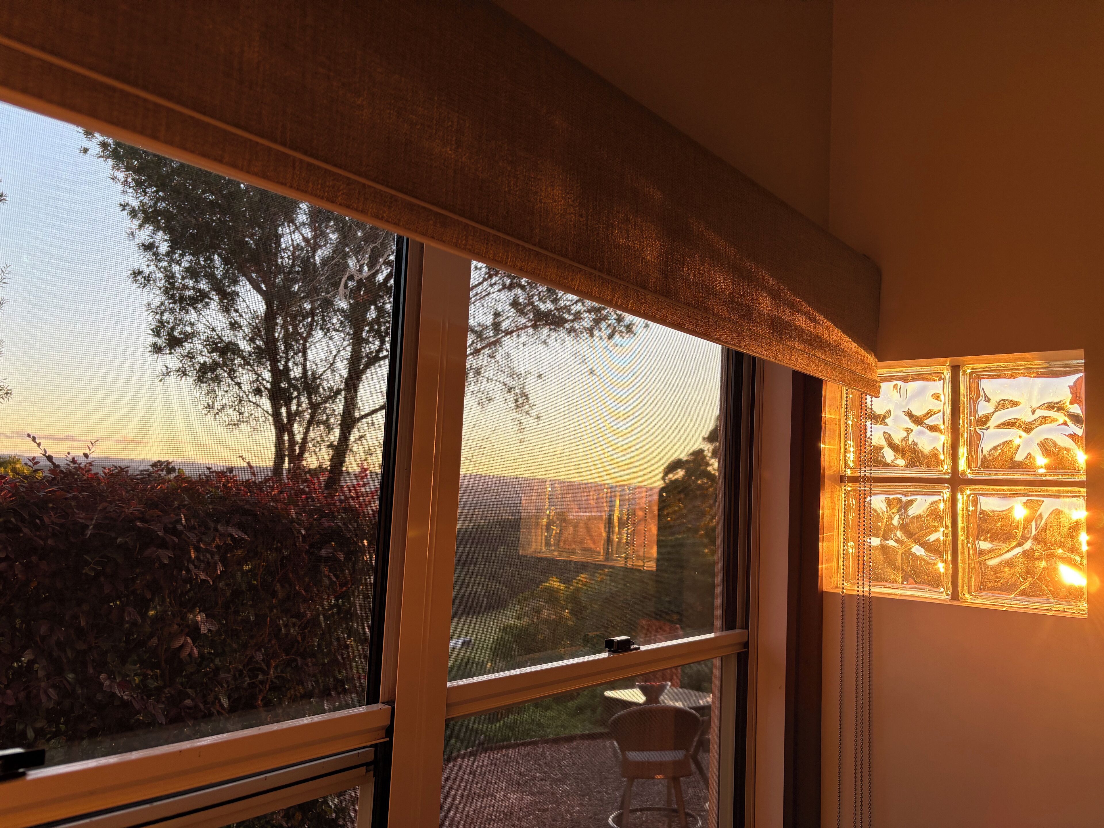 Una habitación con ventanas amplias, vista a árboles y un paisaje lejano, y una lámpara fijada a la pared.