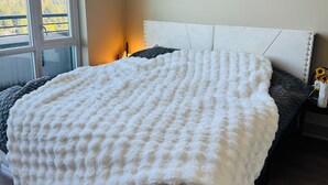 Een slaapkamer met een groot bed, een wit hoofdeinde en uitzicht op een bos door een raam.