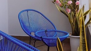 A balcony with two blue chairs, a potted plant, and a decorative vine with pink flowers. - Le Indochina Hotel by AHH Group (Da Nang)