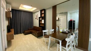 A modern living room with a brown sofa, white chairs, a wooden dining table, and a large mirror. - Le Indochina Hotel by AHH Group (Da Nang)