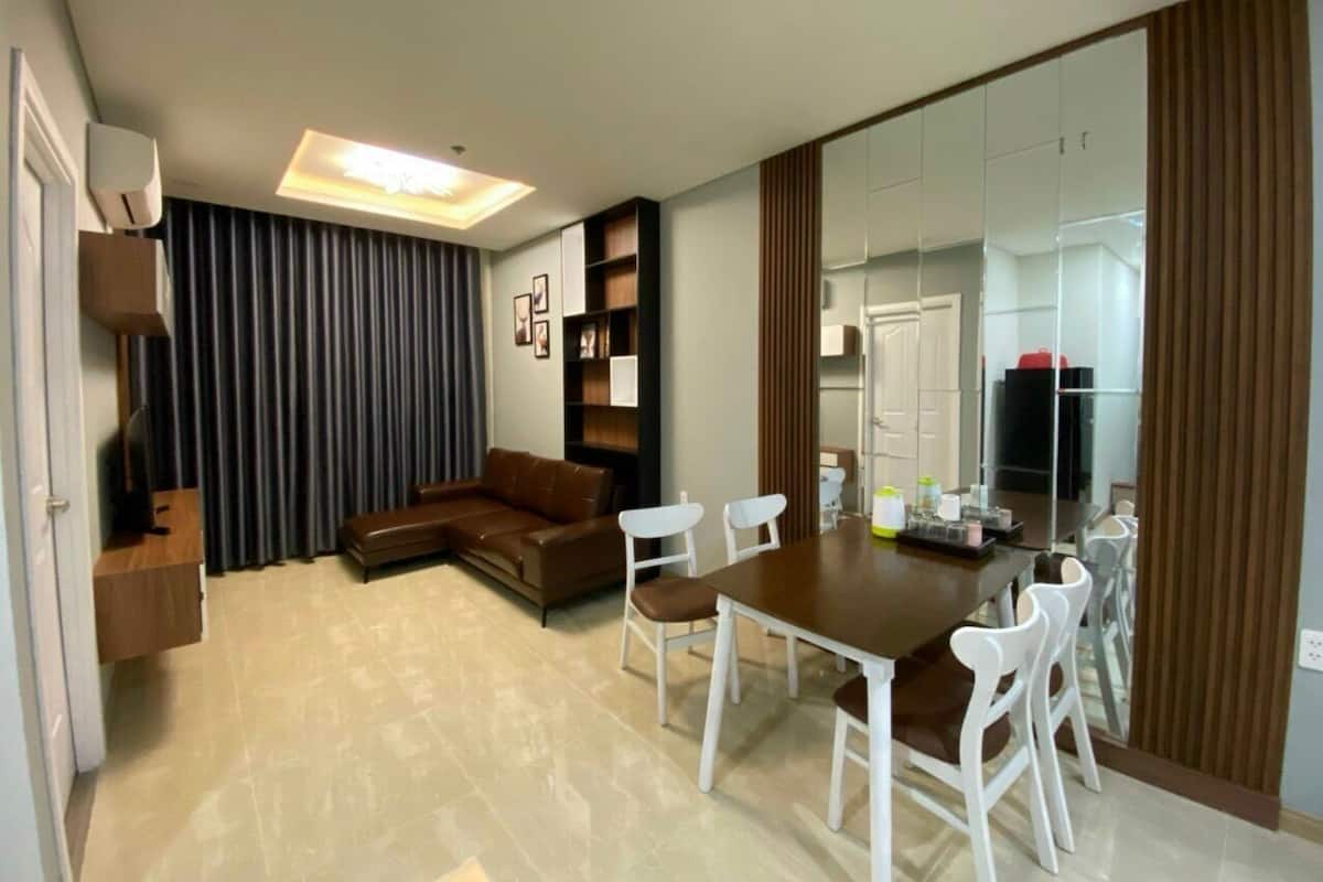 Uma sala de estar moderna com um sofá marrom, cadeiras brancas, uma mesa de jantar de madeira e um espelho grande.