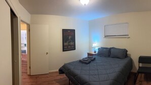 A bedroom with a bed, a poster, a nightstand with a lamp, a chair, and a window with blinds.
