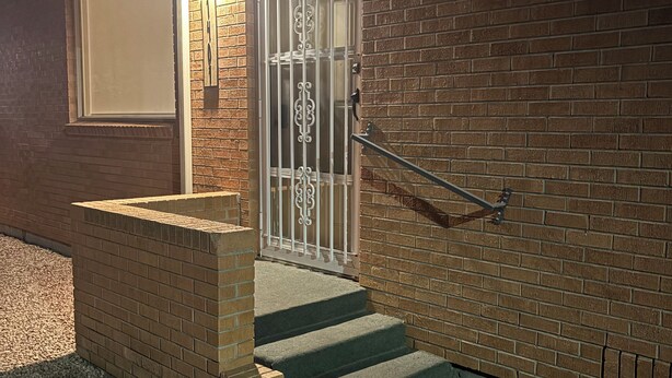 A brick building with a metal gate, steps leading to a door, and a window.