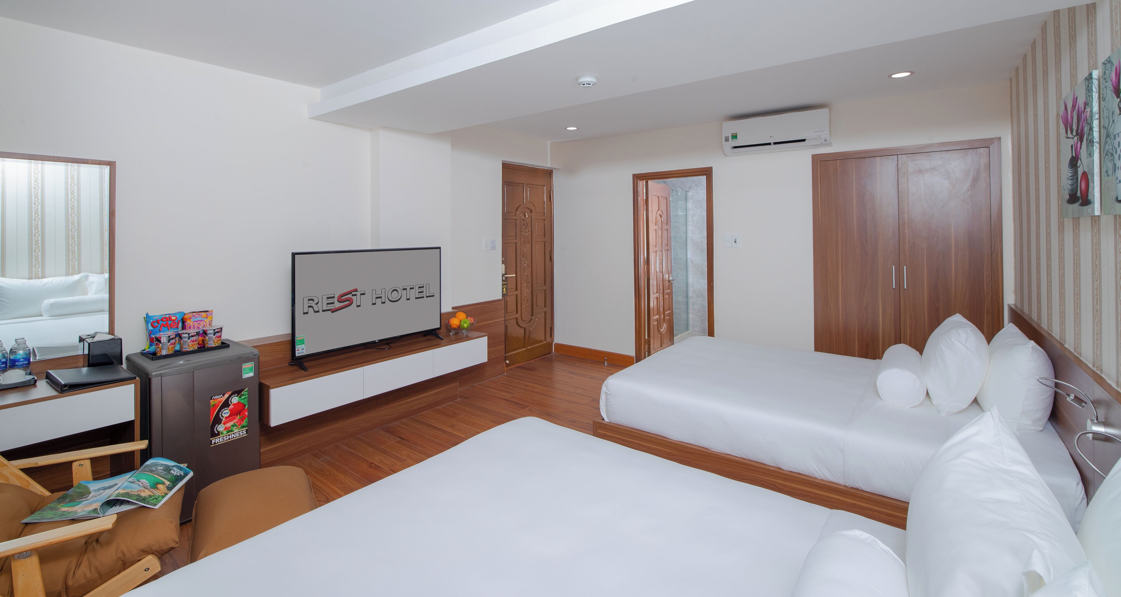 A hotel room with two beds, a TV, a desk with snacks, and a minibar.