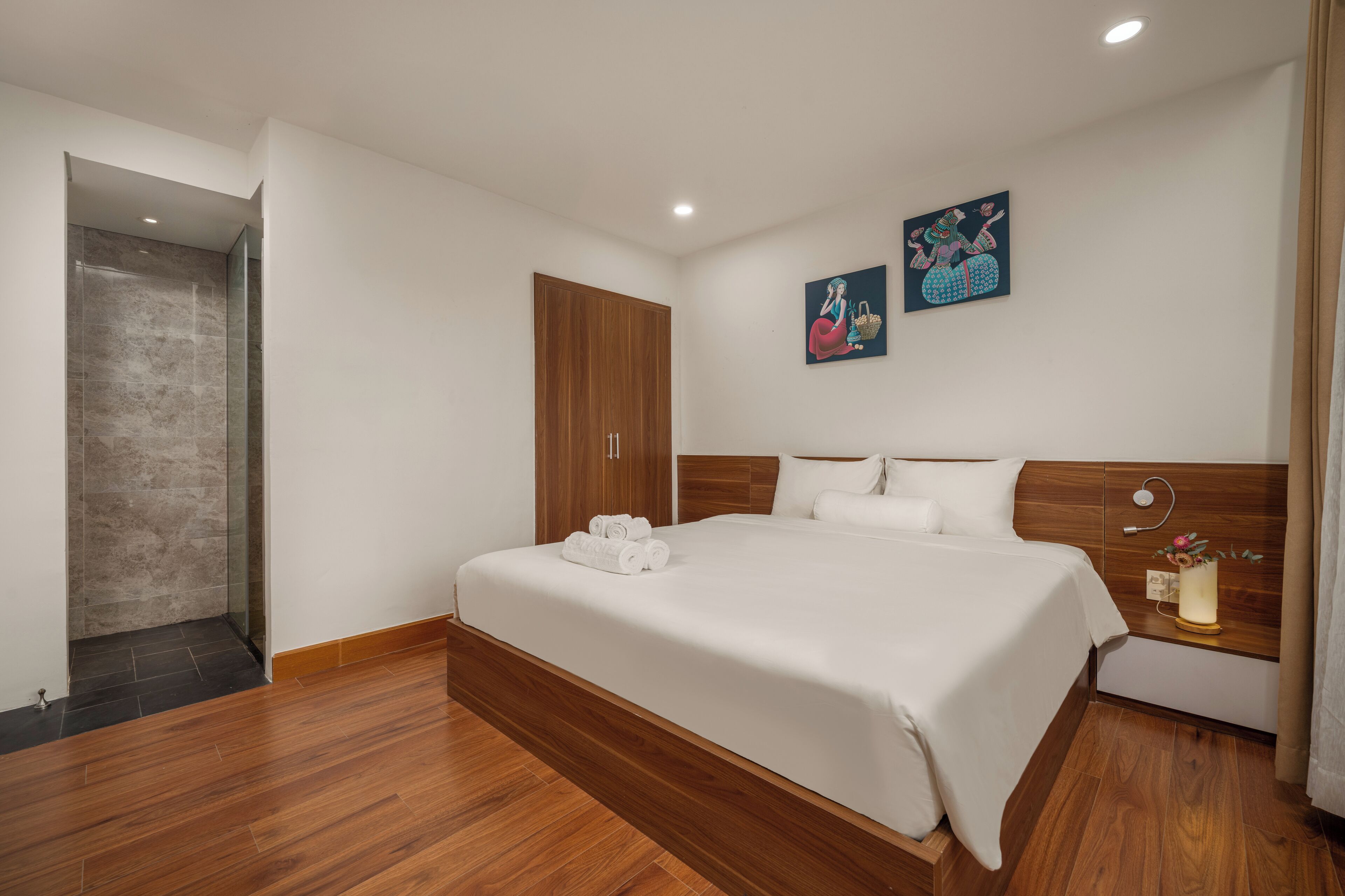 A modern hotel room with a large bed, wooden flooring, a wooden wardrobe, and a shower area.