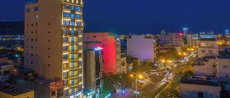 Un hotel de varios pisos con un llamativo letrero que dice 'Rest Hotel', un balcón visible en el segundo piso, y vista a la calle con edificios iluminados y un cielo nocturno despejado.