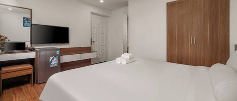 A hotel room with a bed, a desk with a computer and a refrigerator, a television, and a wardrobe.