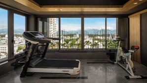 Ein modernes Fitnessstudio mit Laufband, Ergometer und einem großen Fenster mit Blick auf die Stadt.