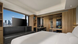 Ein modernes Hotelzimmer mit einem großen Bett, einer Sitzecke, einem Fernseher und Blick auf die Stadt.