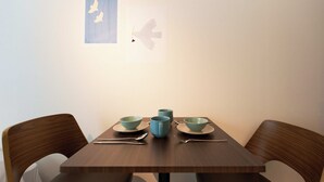 A dining table with three bowls and a mug, accompanied by cutlery, set against a plain wall with two framed bird silhouettes. - Bellie Sangenjaya by Tranova (Tokyo)