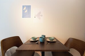 Une table à manger avec trois bols et une tasse, accompagnée de couverts, placée devant un mur uni orné de deux silhouettes d’oiseaux encadrées.