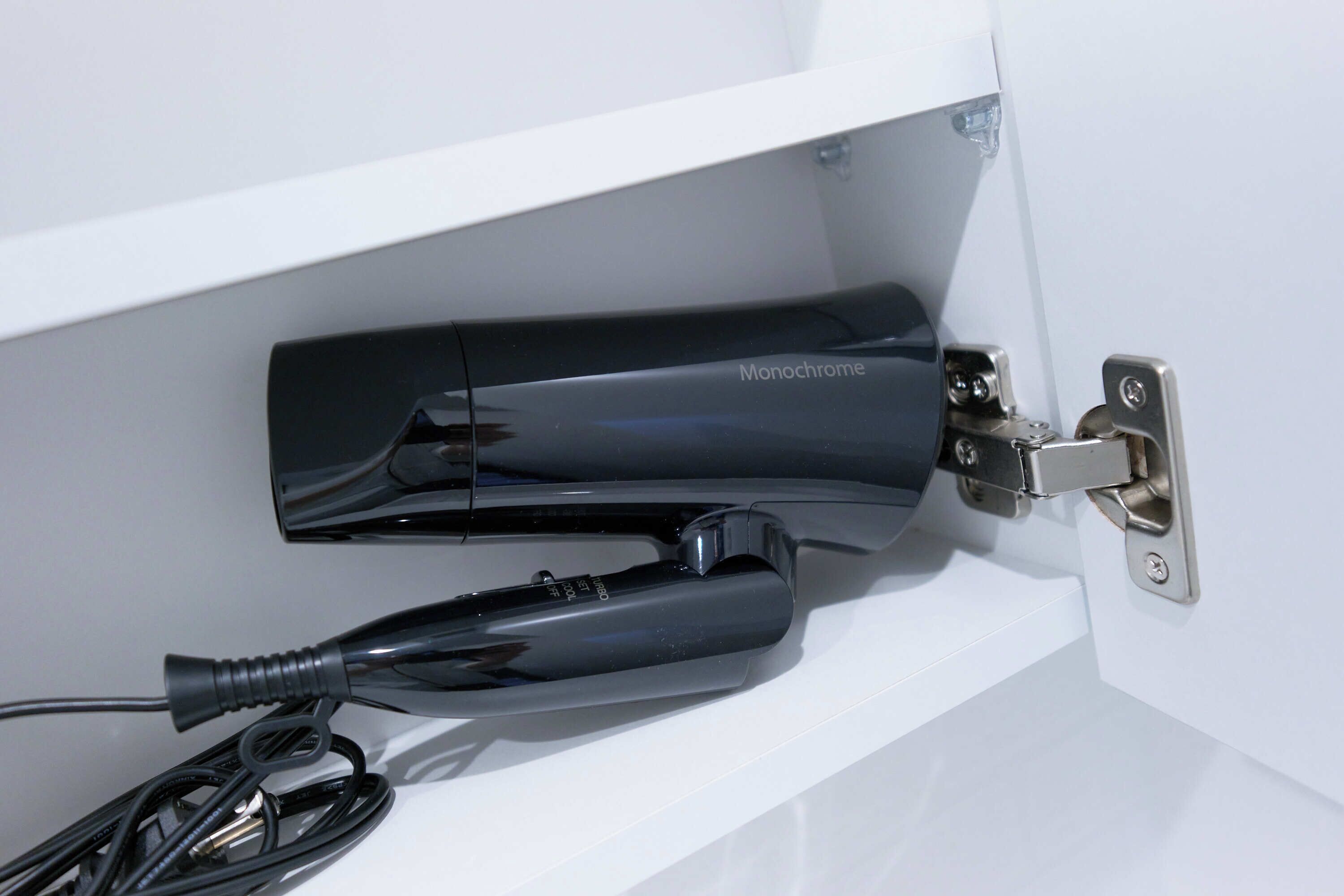 Une étagère blanche sur laquelle se trouve un appareil électronique noir portant l’inscription « Monochrome » et un câble noir.