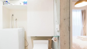 A modern bathroom with a white toilet, a washing machine, and a shower area.