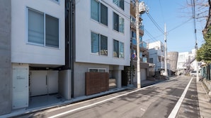 A modern urban street with a white building featuring multiple windows and a gated entrance.