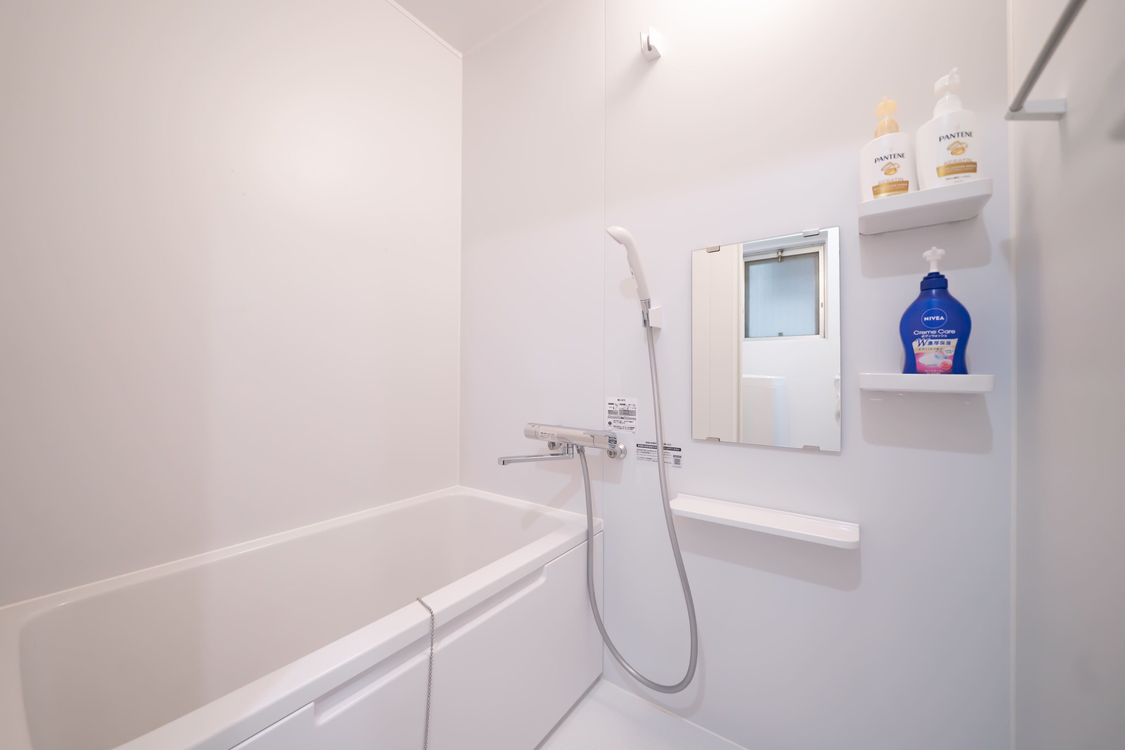 Un baño blanco con bañera, ducha y espejo. Hay repisas con artículos de aseo.