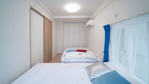 A bedroom with two beds, a wardrobe, a window with curtains, and an air conditioning unit. - Yamamoto Building by Tranova (Tokyo)