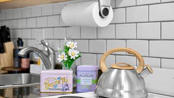 A stainless steel kettle with a wooden handle on a white stove, two tea tins, and a roll of paper towels on a kitchen counter.
