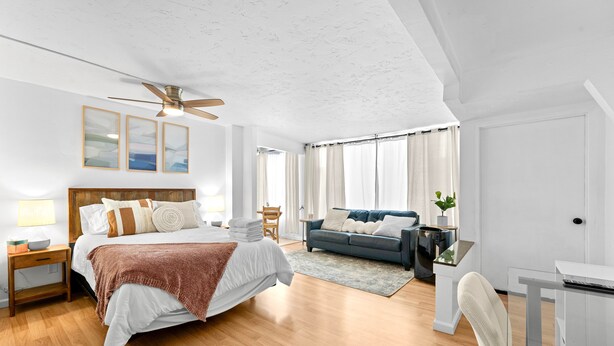 Une chambre moderne avec un grand lit, un bureau, un canapé et un ventilateur de plafond.