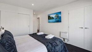 A hotel room with a large bed, a painting of a lake, and a white wardrobe. - Treble Cone Views  - 2 Bedroom Apartment (Wānaka)