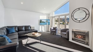 A modern living room with a leather sofa, a round coffee table, and a fireplace. - Treble Cone Views  - 2 Bedroom Apartment (Wānaka)